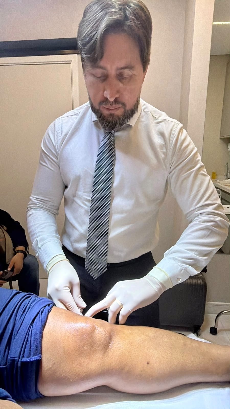 Dr. Denys aplicando infiltração no joelho de um paciente no consultório