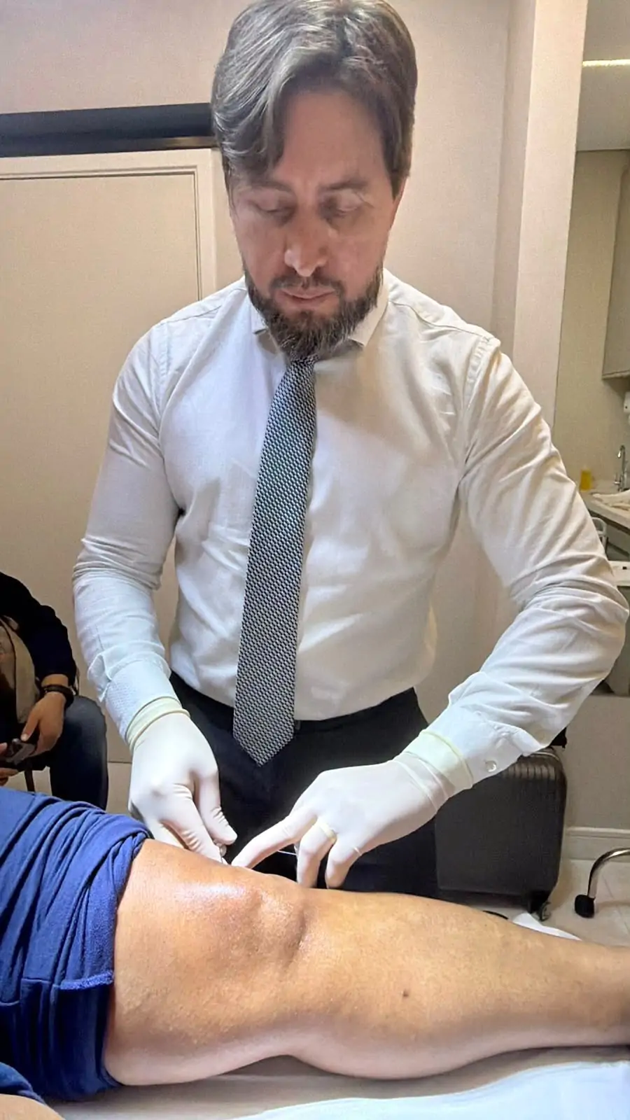 Dr. Denys aplicando infiltração no joelho de um paciente no consultório